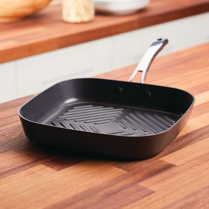 The 11-Inch Cook + Create Hard Anodized Nonstick Deep Grill Pan sits elegantly on the wooden kitchen countertop, showcasing its hard anodized aluminum construction.
