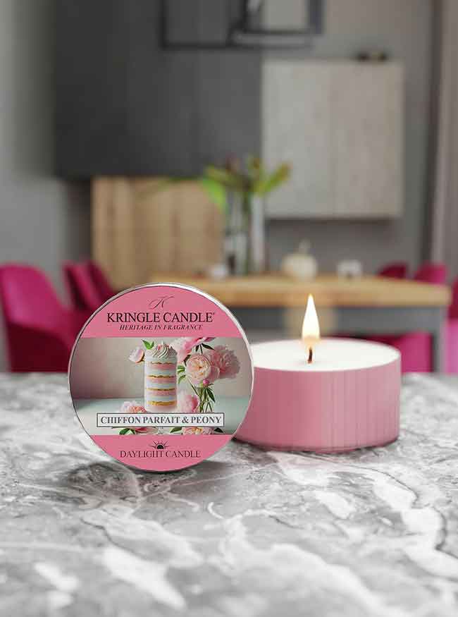 A pink candle labeled "Kringle Candle, Chiffon Parfait & Peony" sits on a marble surface, lit, with a blurred background.