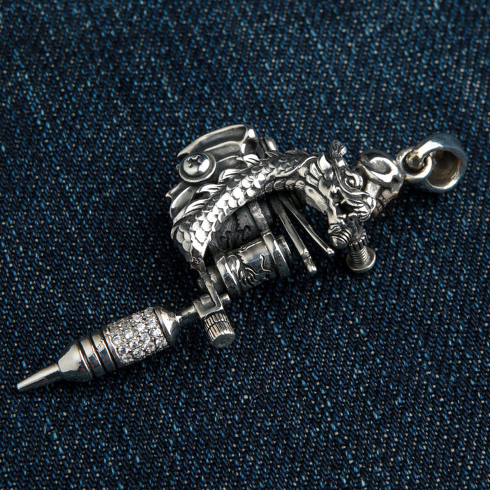 A close-up of the tattoo machine pendant, focusing on the grip that is intricately encrusted with sparkling clear stones.