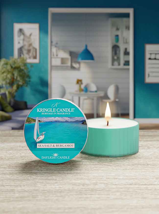 A lit teal candle labeled "Kringle Candle, Sea Salt & Bergamot" sits on a wooden counter.