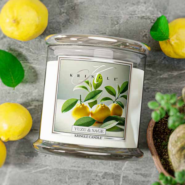 Kringle Candle with Yuzu & Sage flavor surrounded by lemons and a plant on a gray surface
