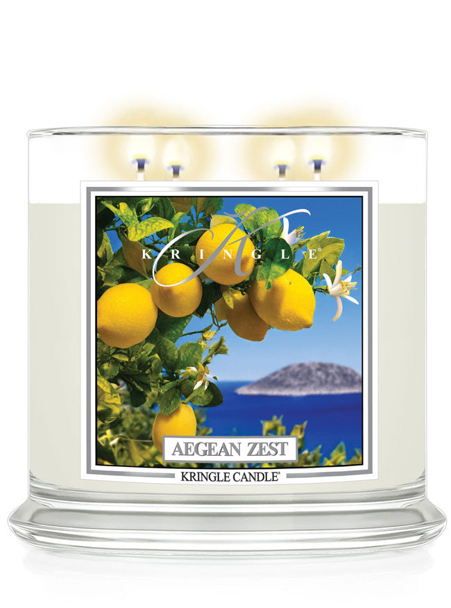 Kringle Candle Aegean Zest 4-Wick Jar Candle – A wide, clear glass jar candle with four lit wicks, filled with white wax. The label showcases vibrant yellow lemons, green leaves, and white blossoms against a deep blue ocean and an island in the background. The ‘Kringle Candle’ logo is displayed at the top, with the fragrance name ‘Aegean Zest’ in bold, and ‘Kringle Candle’ branding at the bottom.