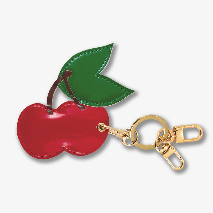Close-up front view of AirTag keychain showcasing cherry-shaped red leather charm and gold keyring on white background
