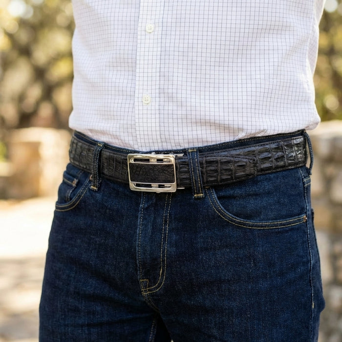 Man wearing black genuine crocodile leather belt with silver rectangular buckle, paired with dark blue denim jeans lifestyle setting