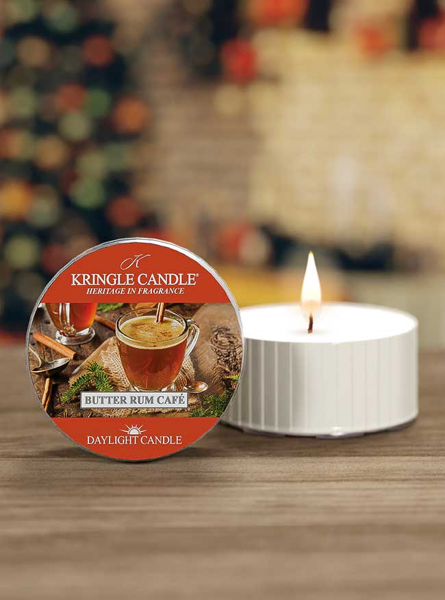 A Kringle Candle labeled "Butter Rum Café" next to a lit, white tea light candle on a wooden surface.
