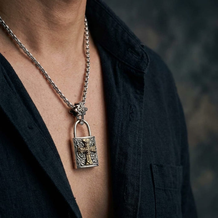 Close-up of a male model wearing a sterling silver gothic padlock pendant necklace featuring an intricate gold Celtic cross design, styled with an open black shirt against a dark background.