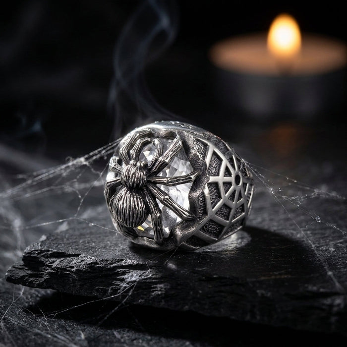 Gothic still-life of the spider ring on black slate with cobwebs and candlelight, clear stone catching the glow