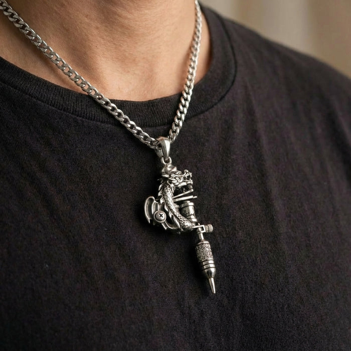 Sterling silver dragon tattoo machine pendant on Cuban link chain worn by man in black t-shirt, featuring detailed dragon sculpture wrapped around miniature tattoo gun design with ornate metalwork