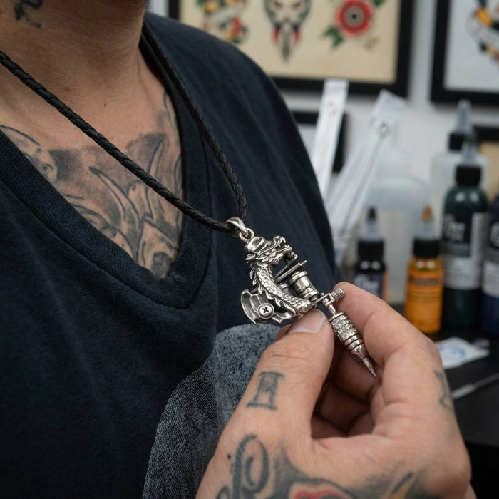 Silver dragon tattoo machine pendant on black braided leather cord worn by tattooed man in tattoo studio, detailed miniature tattoo gun design with dragon motif held in hand showing intricate metalwork