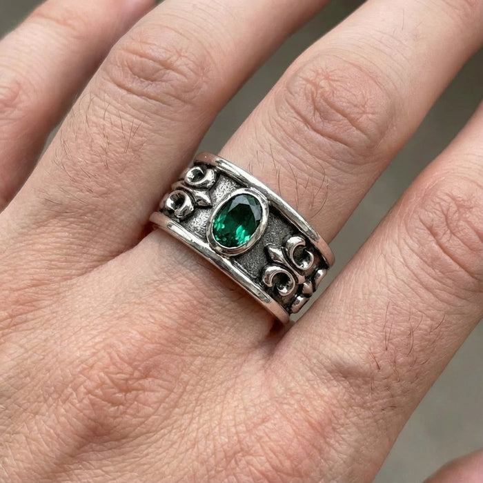 Men's sterling silver Fleur de Lis ring with emerald stone worn on finger