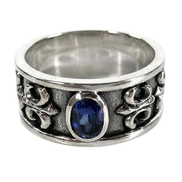 Sterling silver men's band ring featuring a central sapphire-blue oval stone and textured fleur-de-lis side details.