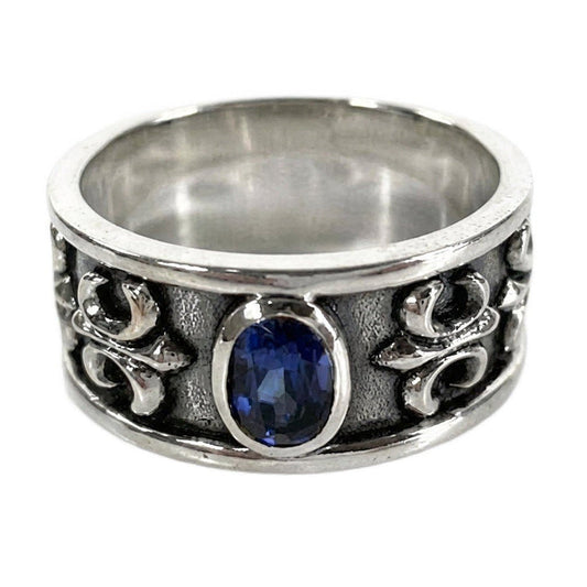 Sterling silver men's band ring featuring a central sapphire-blue oval stone and textured fleur-de-lis side details.