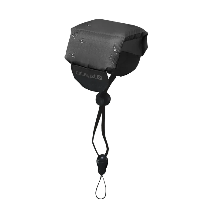 A Stealth Black Floating Lanyard by Catalyst Case US, featuring padding, a drawstring with toggle and clasp for secure attachment, sits against a plain background. The front displays the white "catalyst" logo. Water droplets are visible on the surface.