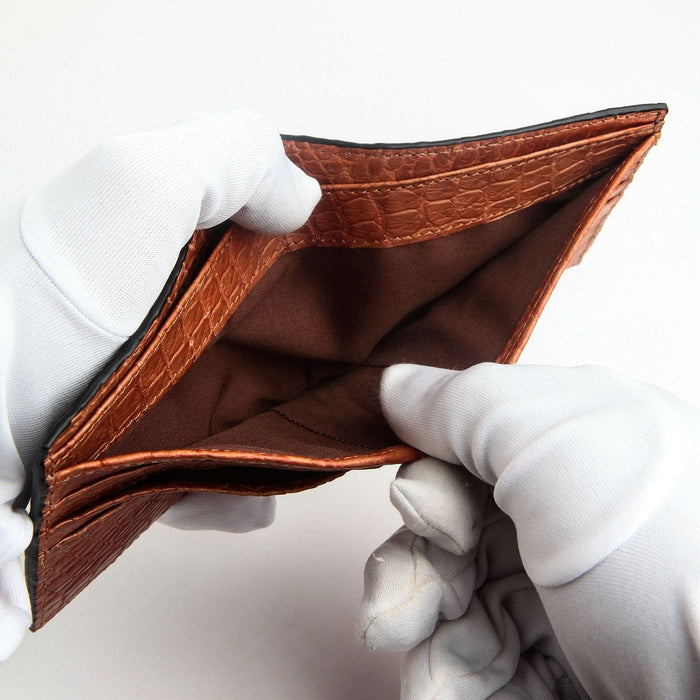White-gloved hands holding open the luxury crocodile wallet to show the spacious bill compartments.
