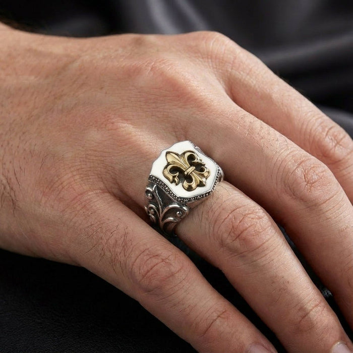 Man's hand wearing a sterling silver shield ring with raised gold fleur de lis motif and baroque scrollwork band