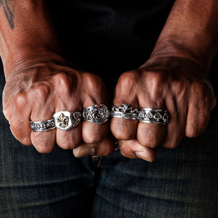 Two clenched fists displaying five sterling silver rings including a gold fleur de lis shield ring alongside dragon and spade motif bands