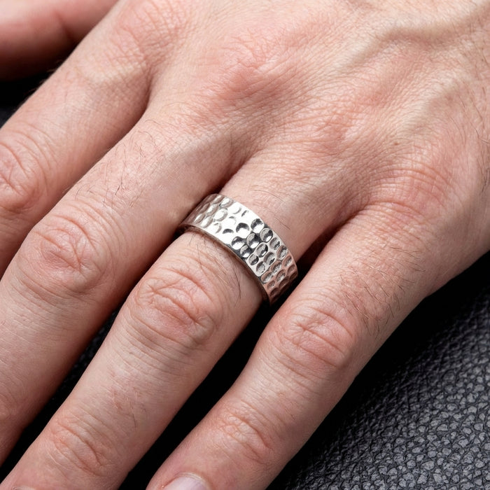 Men's hammered silver band ring with textured dimpled pattern worn on finger, showcasing wide band design against dark leather background