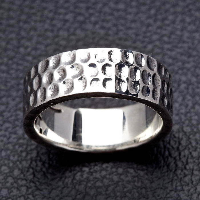 A close-up detail shot of a rugged wedding band, showing the intricate, hand-hammered texture of the solid sterling silver.