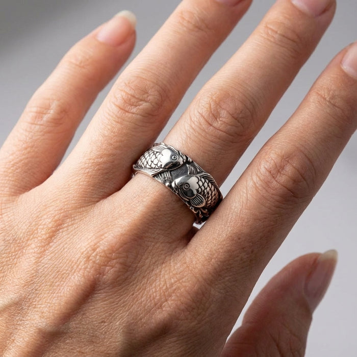 Close-up of a Japanese Koi fish sterling silver ring worn on a model's middle finger, featuring detailed engraved scales and two swimming fish with an oxidized finish.