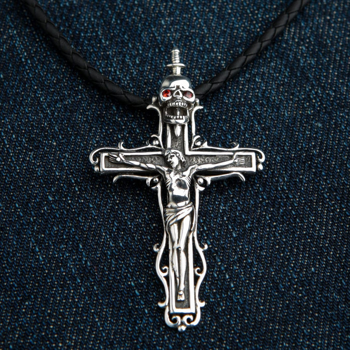 Black braided leather cord attached to the silver crucifix and garnet-eyed skull pendant, resting flat on dark blue denim.