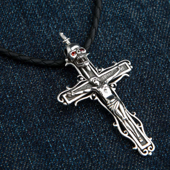 Detailed view of the ornate sterling silver crucifix on denim, highlighting the Jesus figure and red garnet skull eyes.