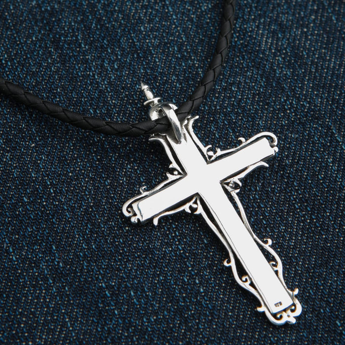Polished reverse side of the silver cross pendant featuring ornate edges and a 925 hallmark, strung on a braided cord.