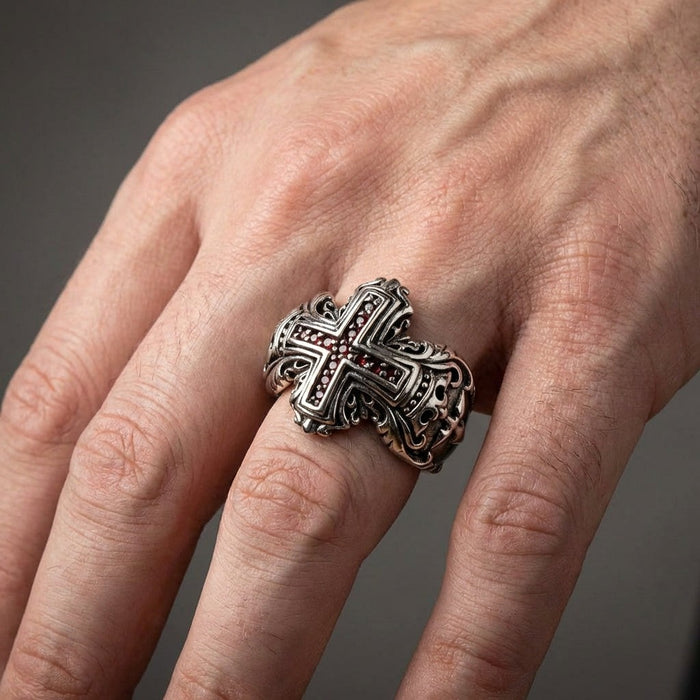 Handcrafted medieval cross ring worn on finger displaying bold sterling silver design with garnet stones