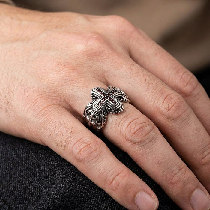 Men's sterling silver cross ring with red garnets worn on hand against dark fabric background