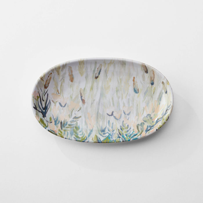A round melamine trinket tray with an ocean and marsh scene in shades of blue and green.