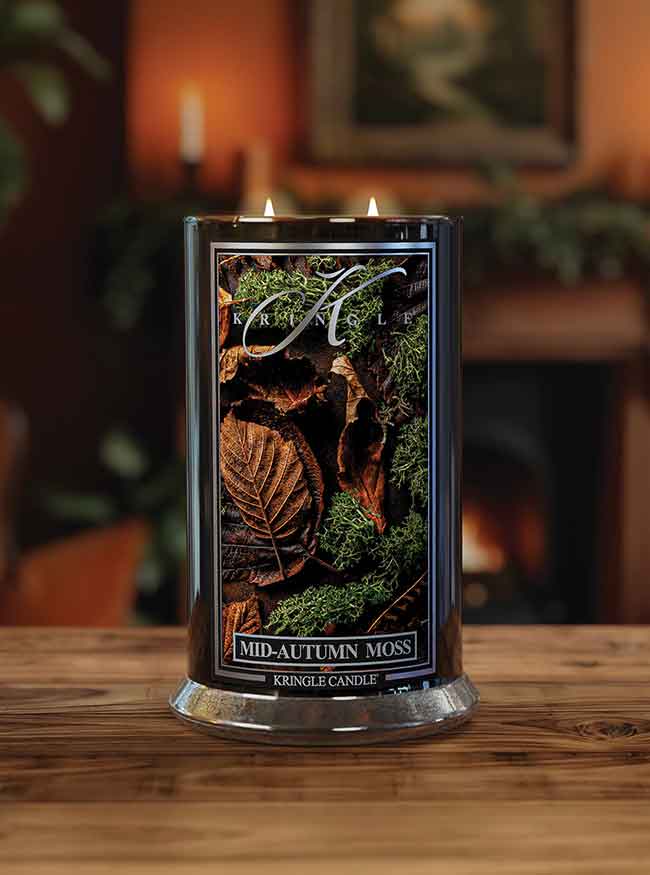 A lit candle labeled "Mid-Autumn Moss" sits on a wooden table, with a cozy, blurred background.