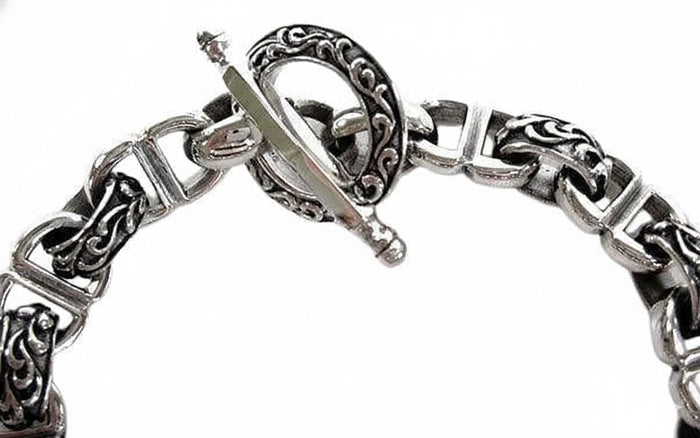 A close-up of the decorative T-bar clasp on the ornate scrollwork bracelet.
