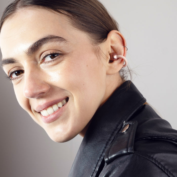 A woman wearing the rose gold Pebbles Air earbuds while smiling.