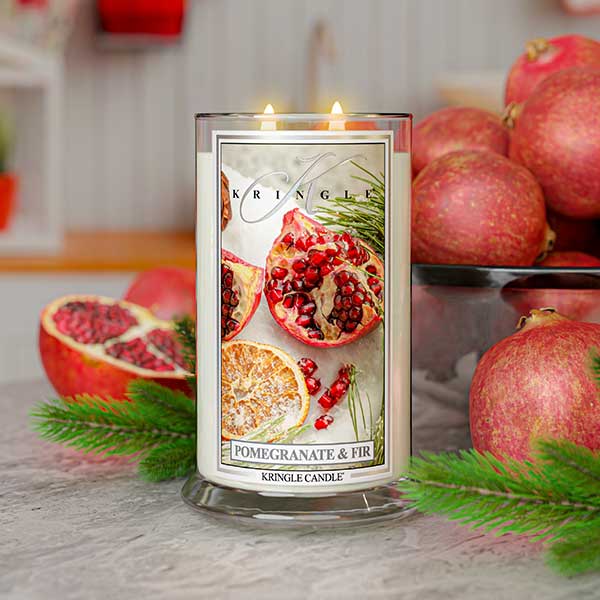 Kringle Candle with pomegranate and fir design surrounded by pomegranates and greenery.