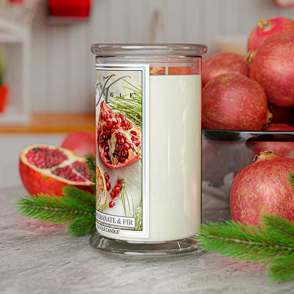 Candle with pomegranate and fir design on a table with pomegranates and greenery.