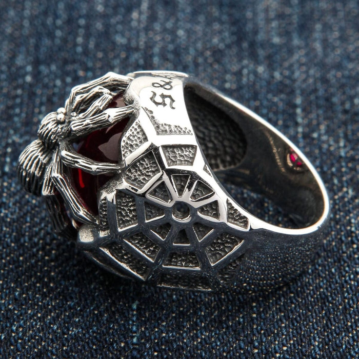 A detailed close-up of the red CZ stone at the center of the intricate sterling silver spider web.
