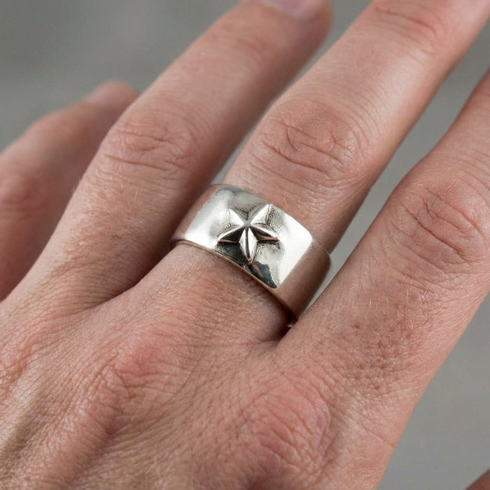 Close-up of a wide polished sterling silver ring featuring a raised five-pointed star design worn on a man's middle finger.