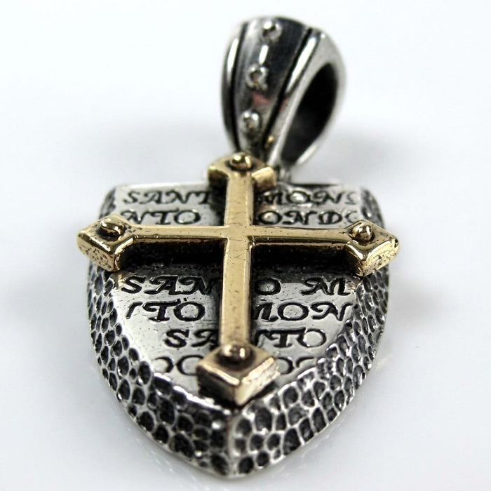 Angled close-up of the two-tone shield pendant emphasizing the warm brass cross, engraved text, and dimpled silver edges.