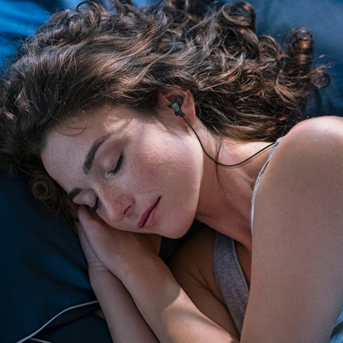 Woman sleeping with SleepTones silicone sleeping earbuds on a blue pillow covered in blue sheets