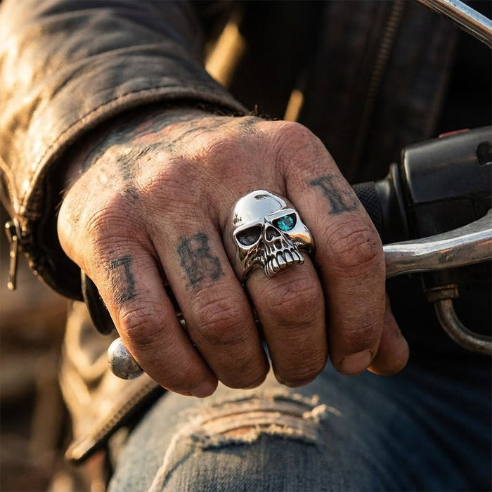 Sterling silver skull ring with blue topaz eye worn on tattooed hand gripping motorcycle handlebar