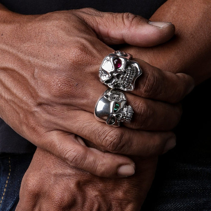 Two handcrafted sterling silver skull rings with gemstone eyes worn on clasped hands