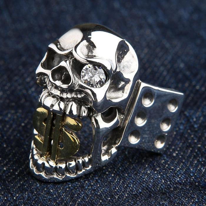 An angled view of the heavy silver gambler's skull ring with a gold dollar sign, on a denim background.
