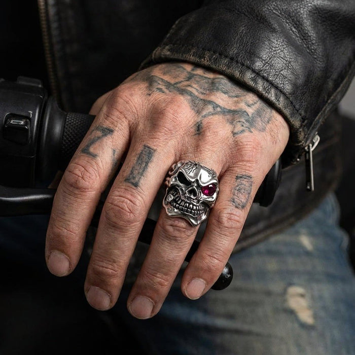 Tattooed hand in a leather jacket gripping a motorcycle handlebar, showcasing the silver mafia skull ring with a red eye.