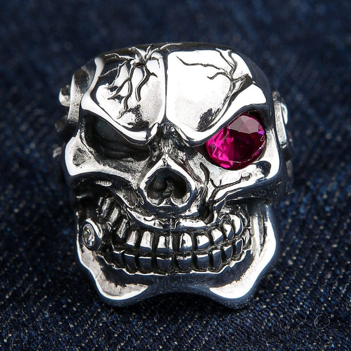 Close-up resting on blue denim, highlighting the cracked silver forehead, bright ruby red eye, and jeweled cigar detail.