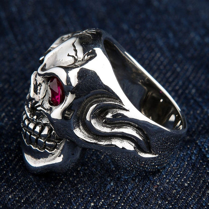 Rear angled perspective highlighting sweeping flame engravings on the thick silver band, a cracked forehead, and ruby eye.