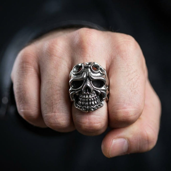 Man wearing sterling silver tribal skull ring on middle finger with closed fist against dark background