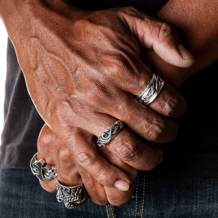 Model with crossed arms wearing multiple silver biker rings and tribal band