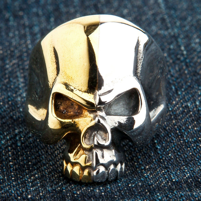 Straight-on view of the two-tone skull ring on denim, displaying the stark contrast of the brass and sterling silver halves.