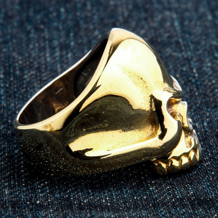 Overhead perspective emphasizing the smooth, polished brass forehead of the two-tone skull ring on dark denim.