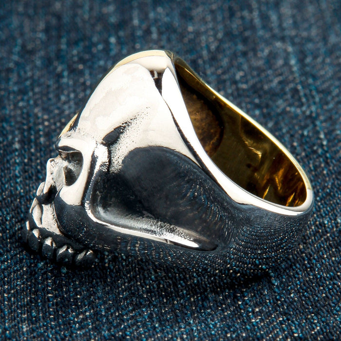 Lying on its side to reveal the thick sterling silver shank and hollow interior of the skull ring on dark denim.