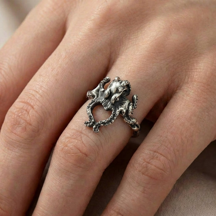 Close-up of a detailed oxidized silver octopus ring worn on a woman's ring finger, showing textured tentacles wrapping around the finger.